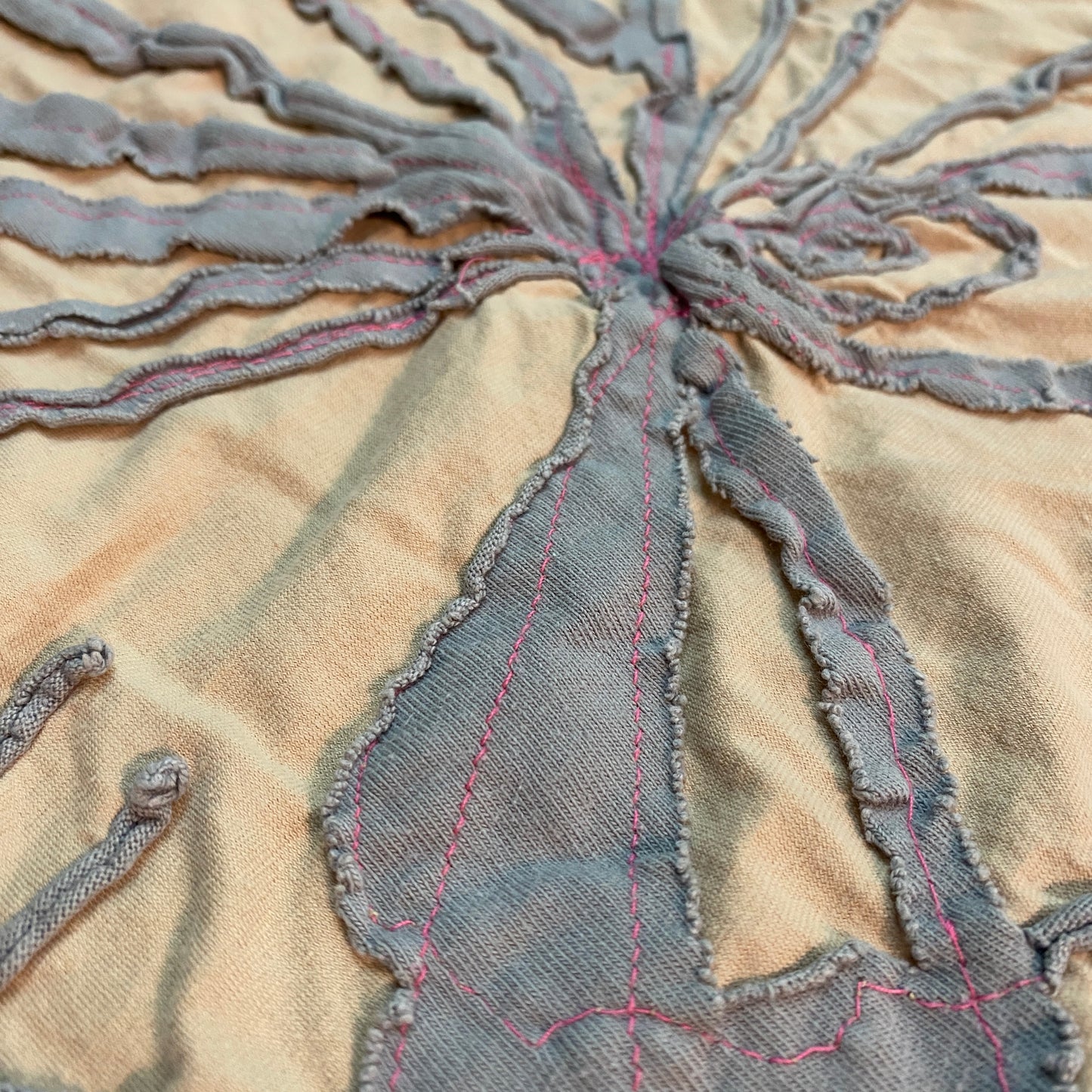 Close up of the peach and grey with hot pink stitching bandana. The edges of the gray fabric curl up because it is a knit fabric.