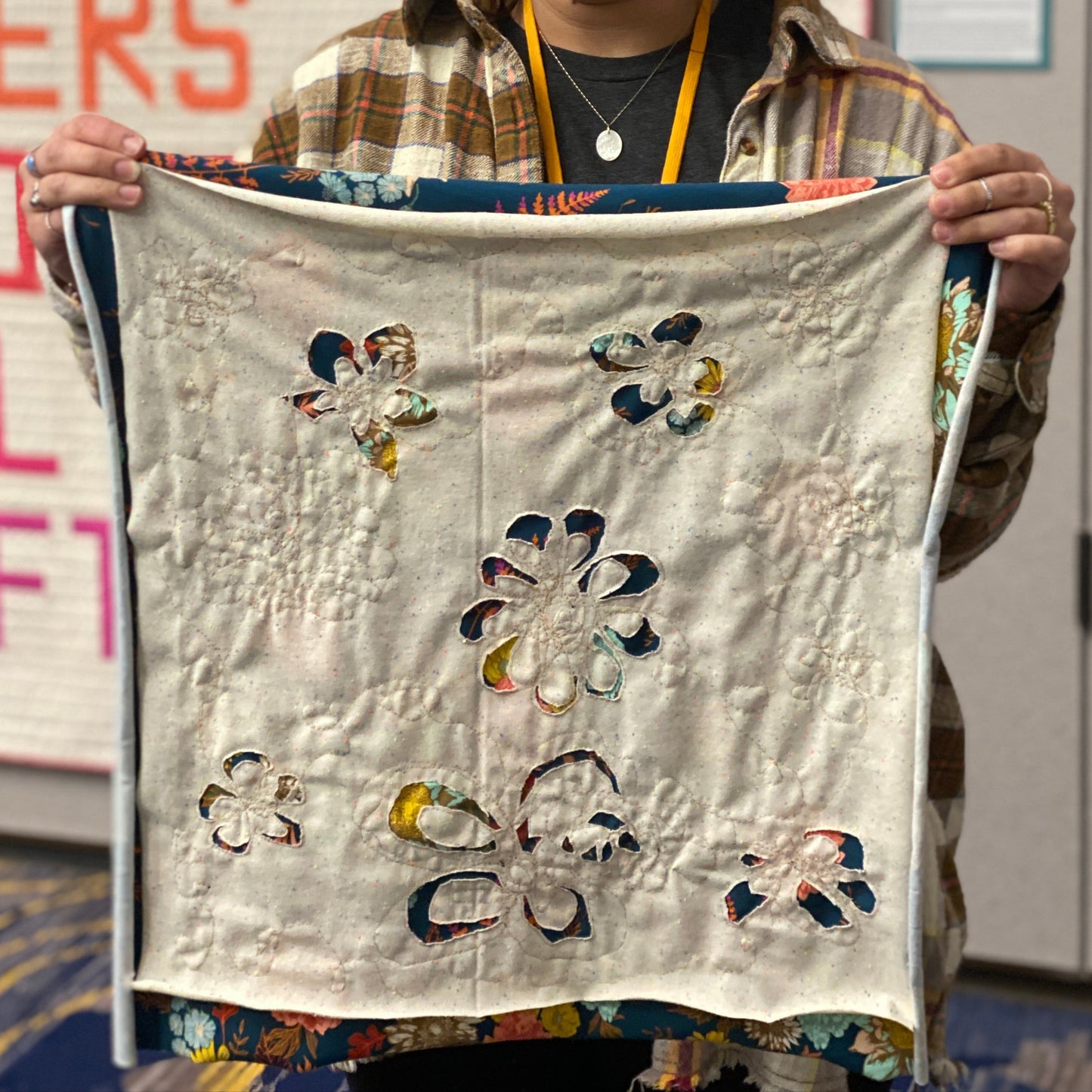 A person is holding up a bandana project that is in progress.