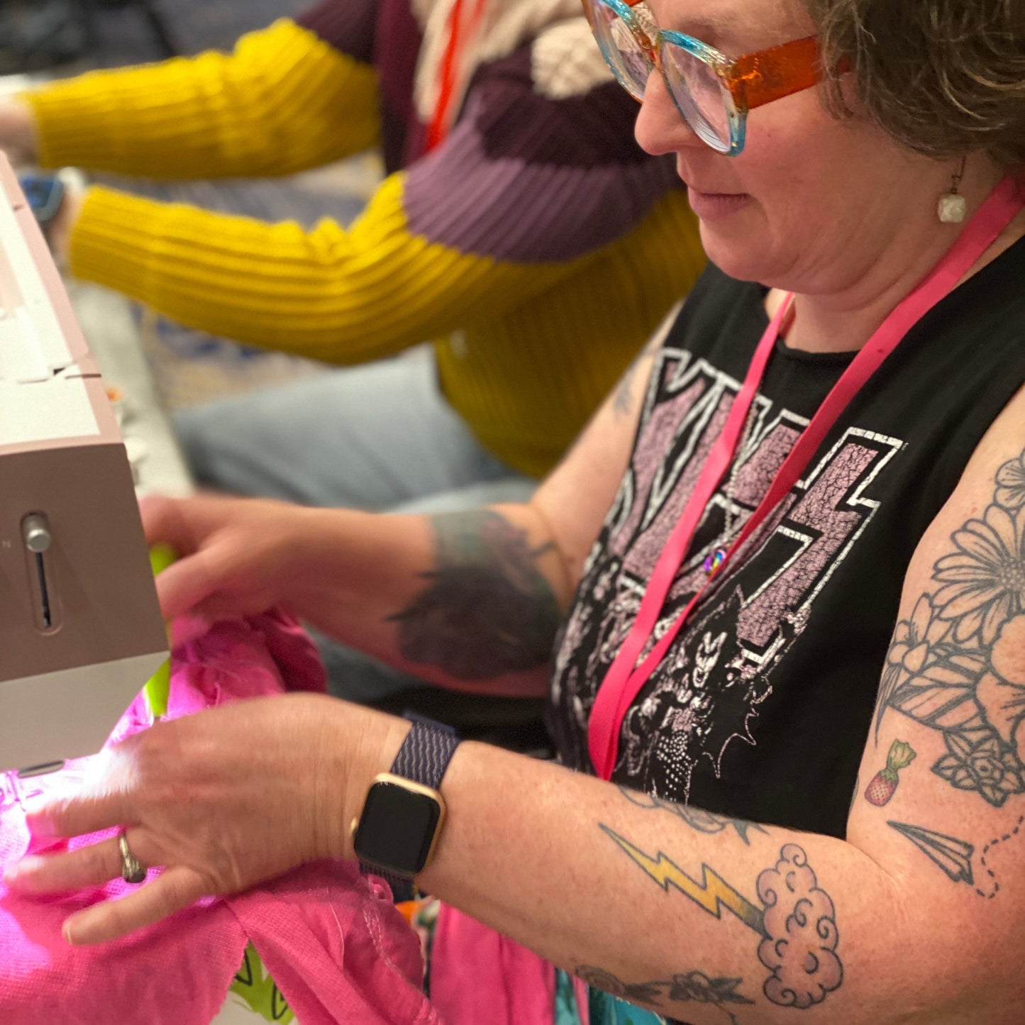 A person is sitting at a sewing machine and working on their hot pink applique bandana.