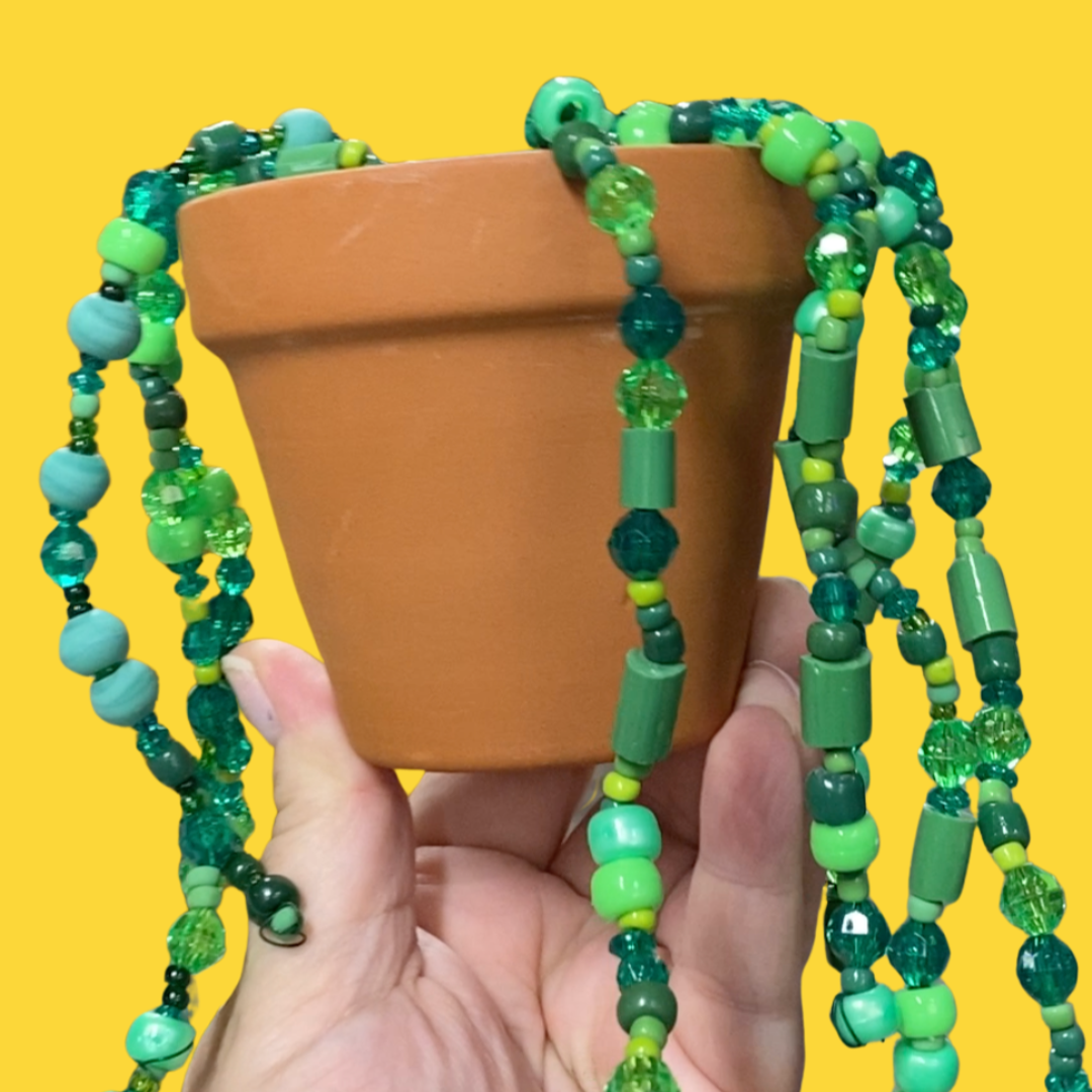 A hand is holding up a terracotta pot with a green, sparkly beaded plant inside.
