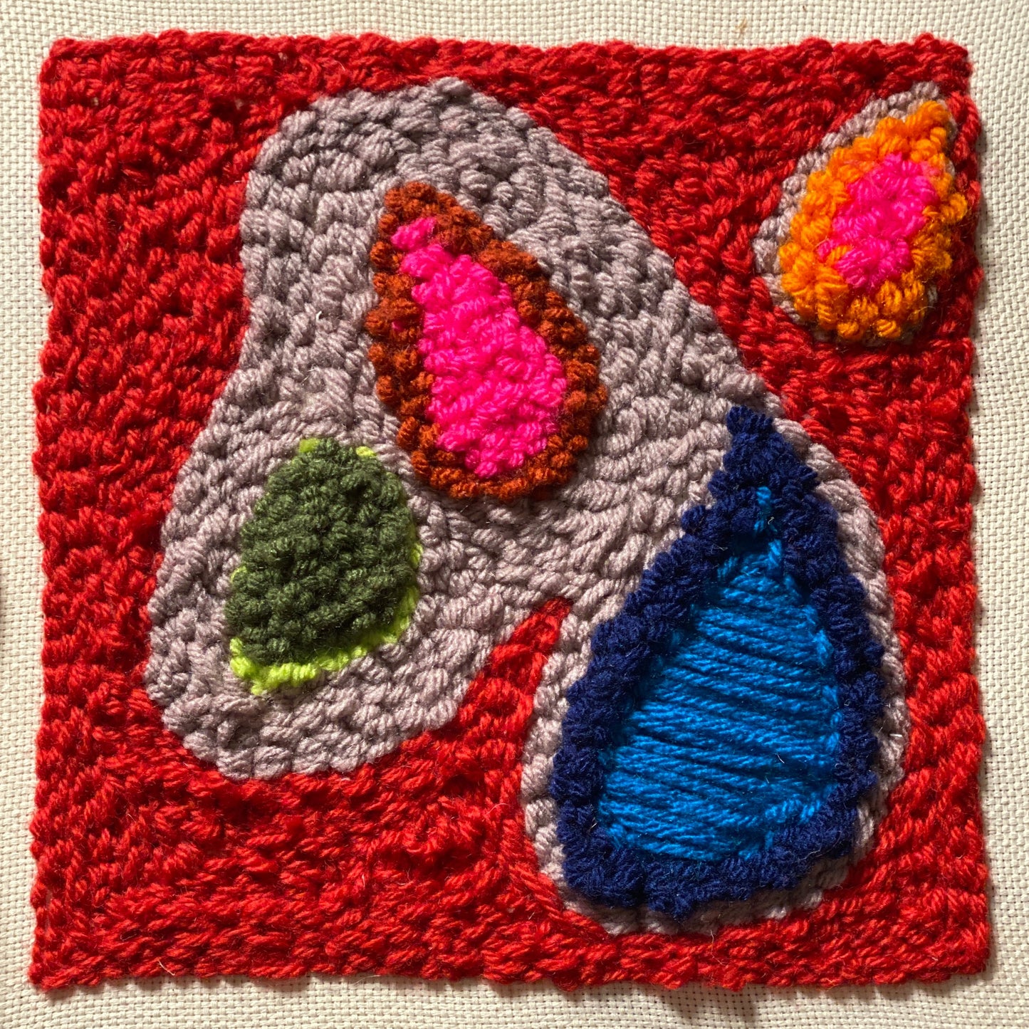 Example of square punch needle wall hanging. This piece shows three different stitches. The background is right red and the interior is made up of pink, orange, green and blue droplet shapes.