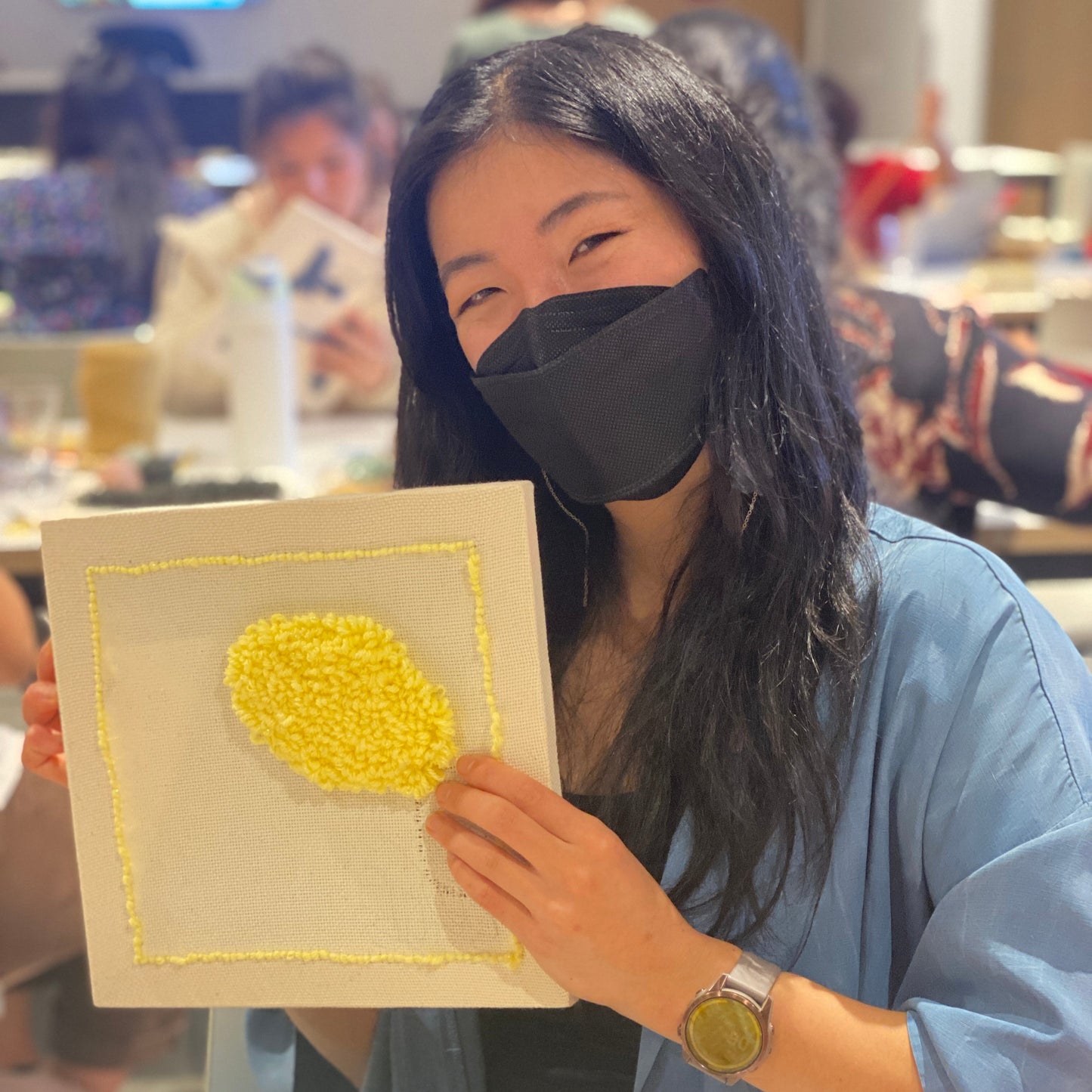 A person is holding up their punch needle canvas project with a bright yellow circle in the upper right corner.