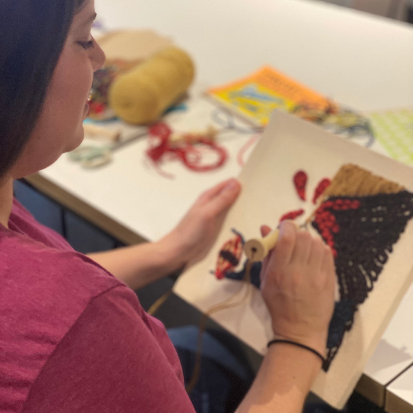 The camera view is pointed over the shoulder of a person working on their punch needle canvas project.