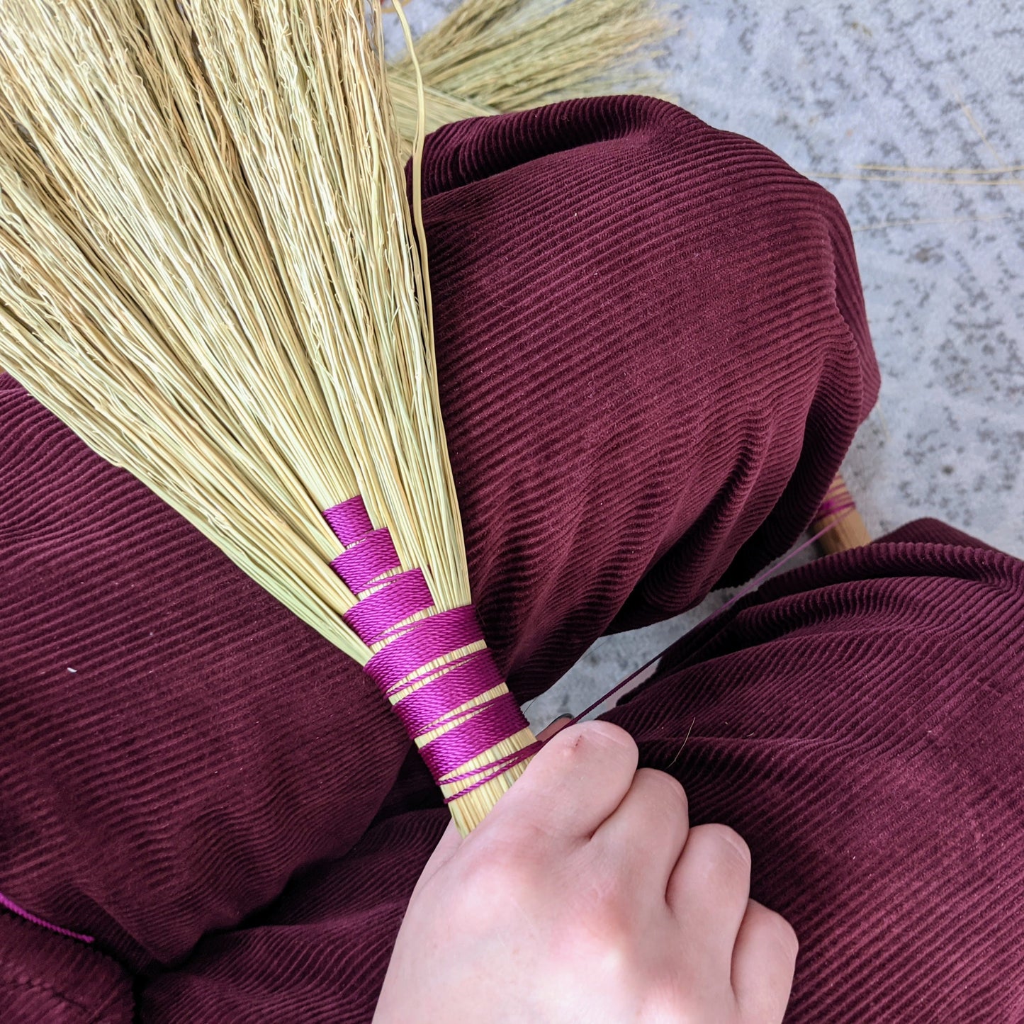 Example of a hand broom. A person is holding it. They are wearing corduroy pants and the detail of the hand broom is in a coordinating magenta color.