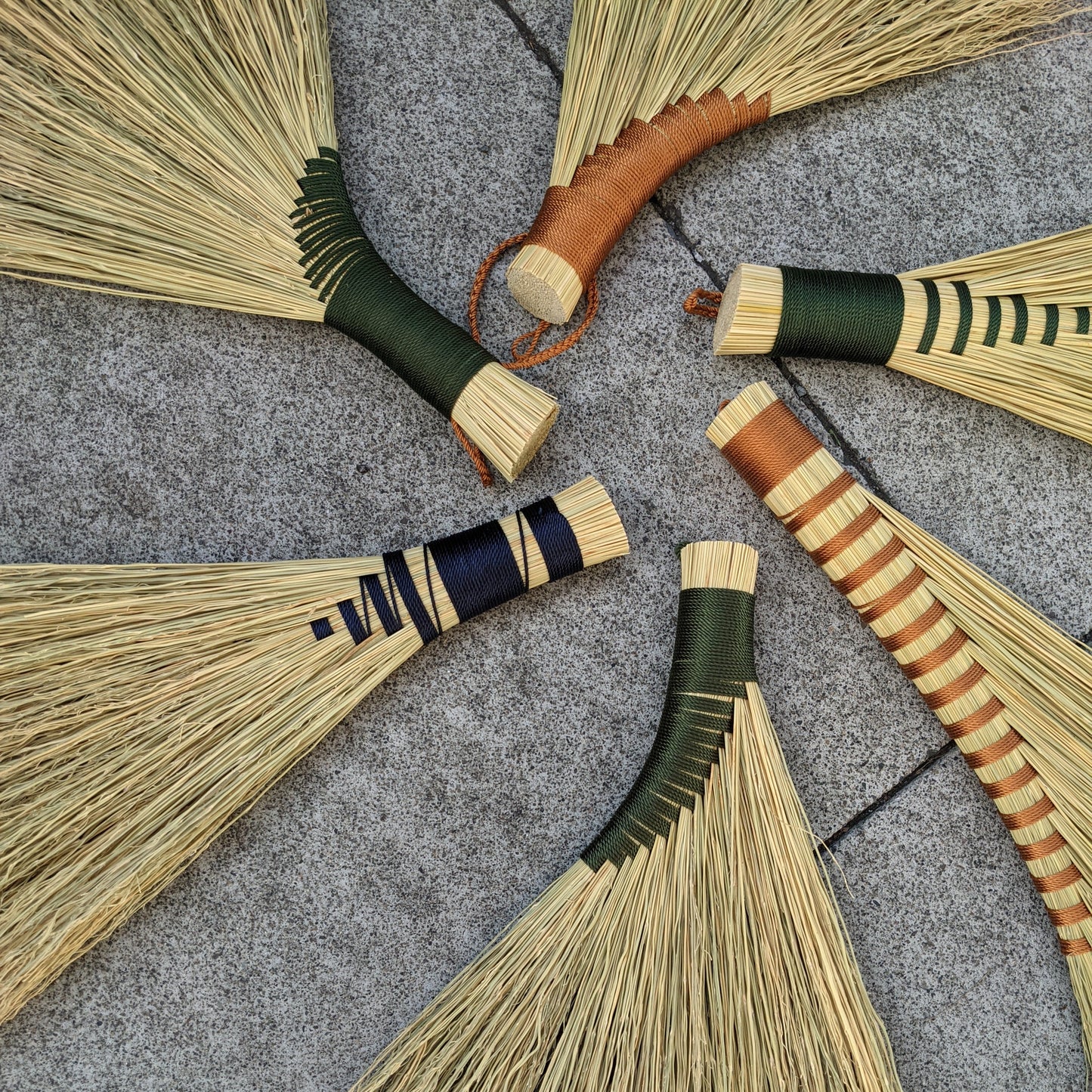 Examples of different types of hand brooms displayed in a circle with their handles pointing inside. There are some with black detail and others with brown detail.