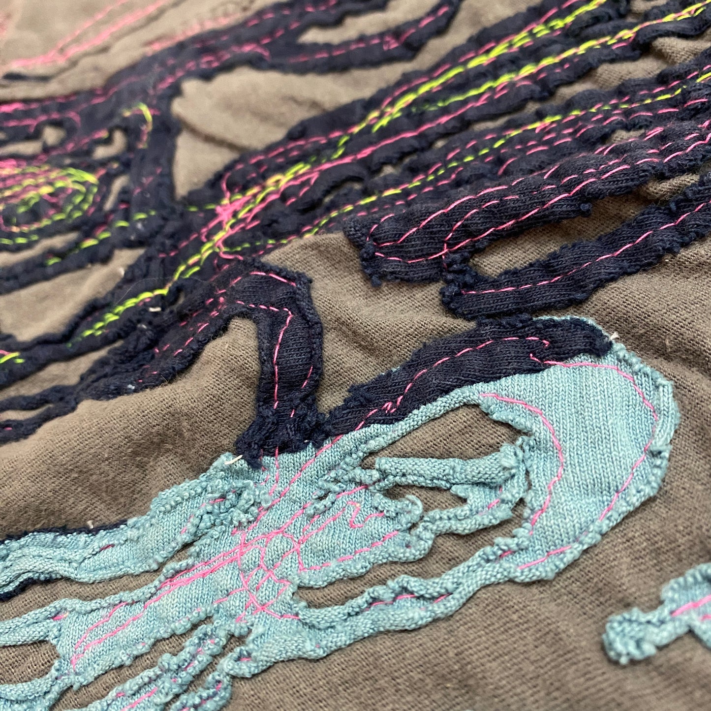 This negative reverse applique bandana has a gray background and a light and dark blue foreground fabric. The top stitching is hot pink and neon yellow.
