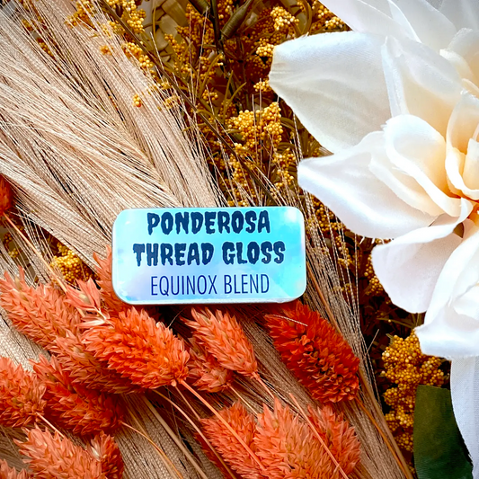 A tin of Ponderosa Thread Gloss - Equinox Blend - against a background of orange, cream and brown dried flowers.