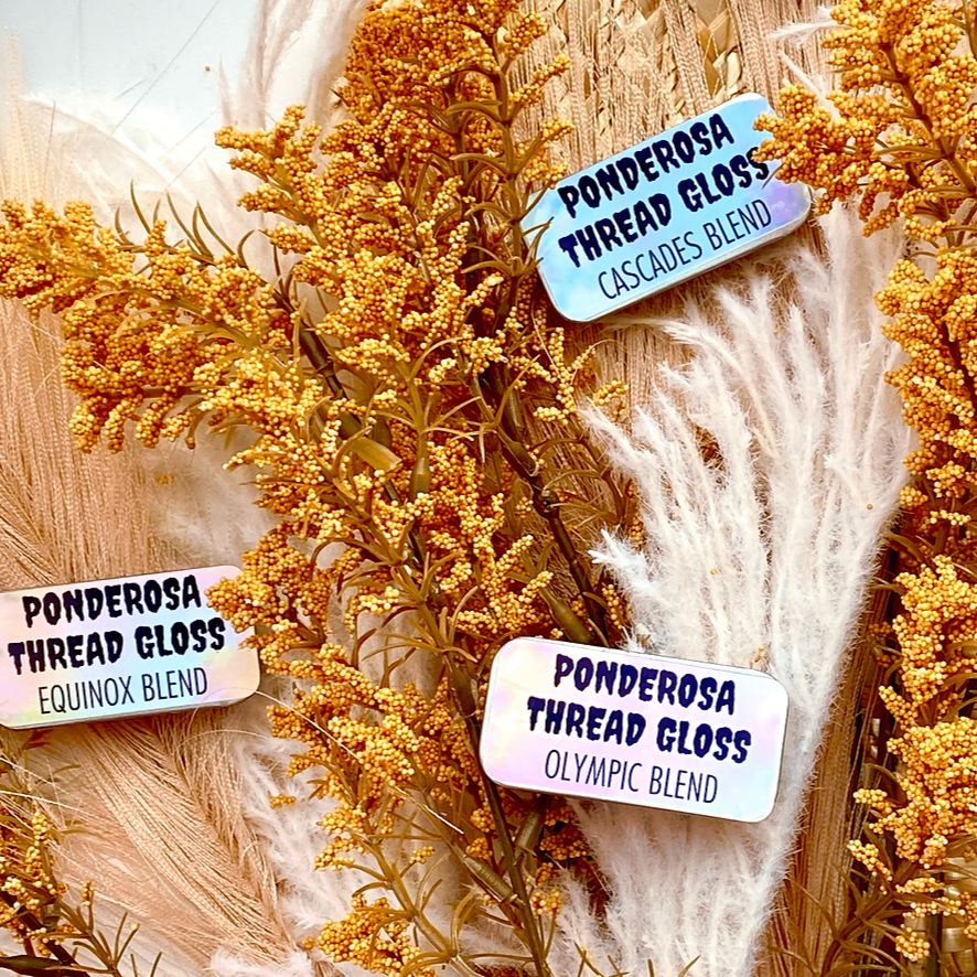Several tins of Ponderosa Thread Gloss scattered onto a background of dried florals.
