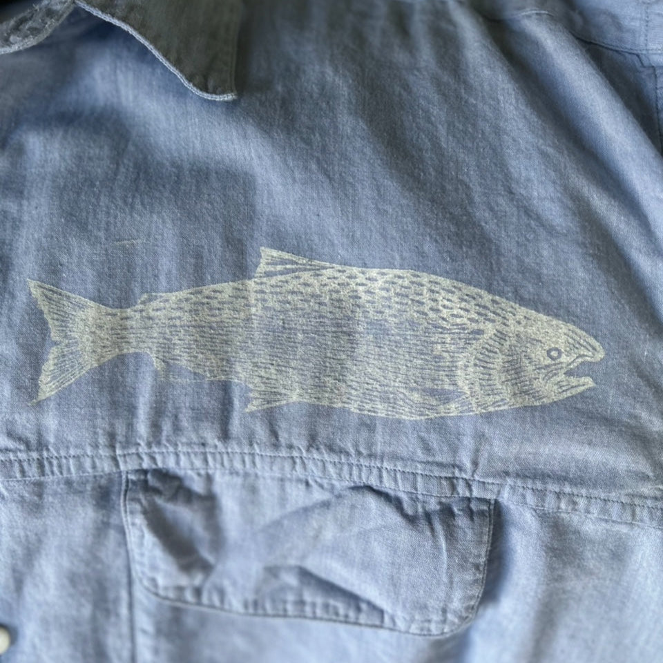 A denim shirt with a fish block printed in white above the pocket.