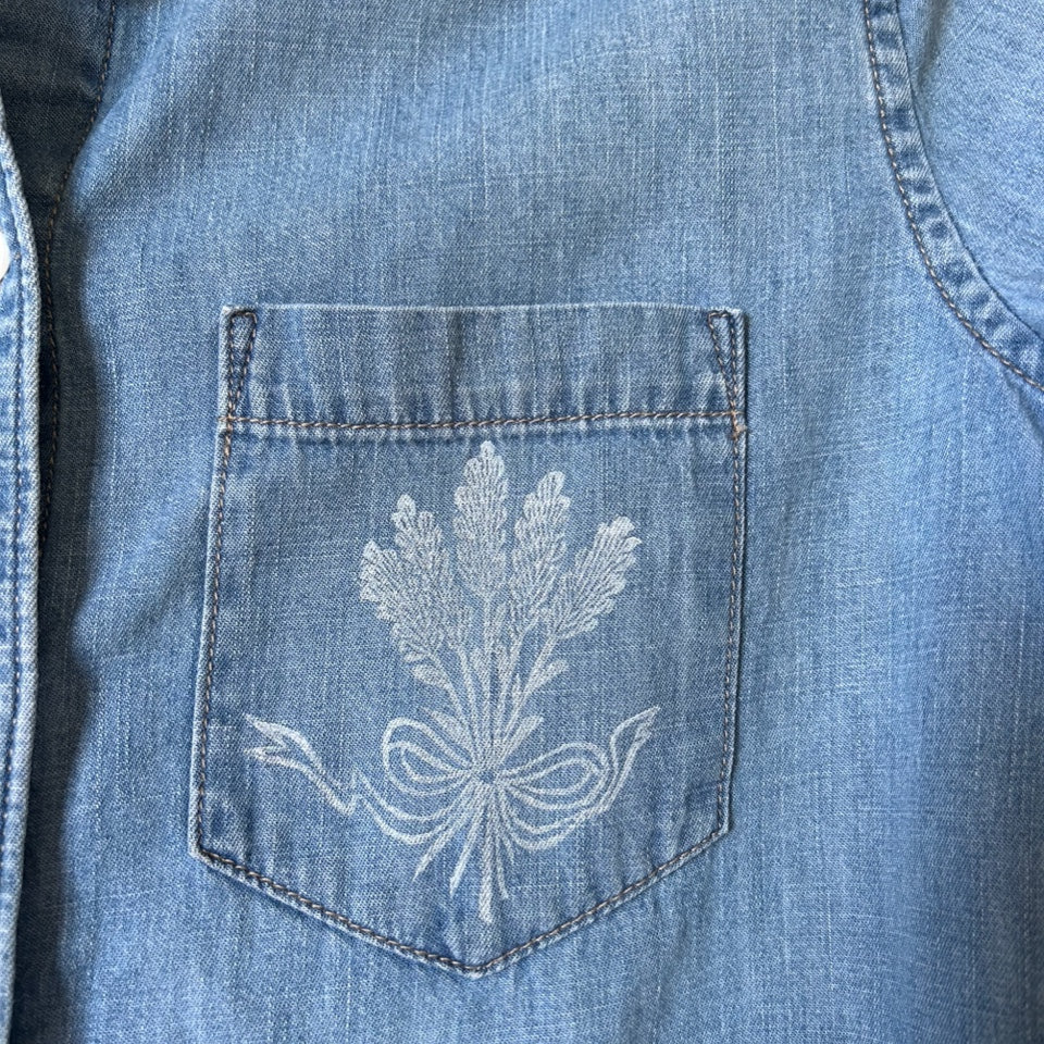 A batch of lavender gathered with a sweet ribbon is block printed on the pocket of a denim shirt with white ink.