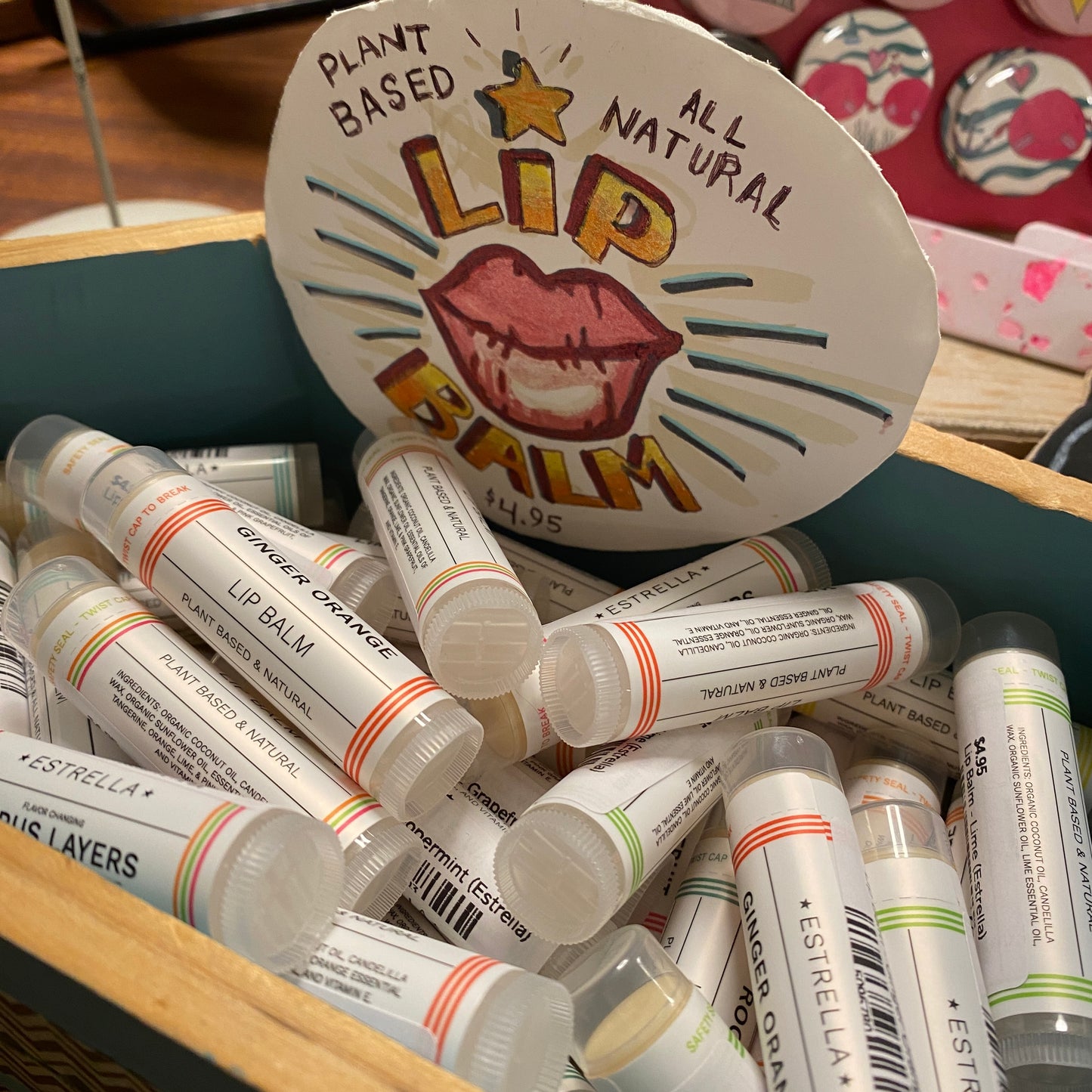 A wood box filled with lip balms. A cute sign is attached that says it is plant based and all natural. It has some cute lips drawn in marker.