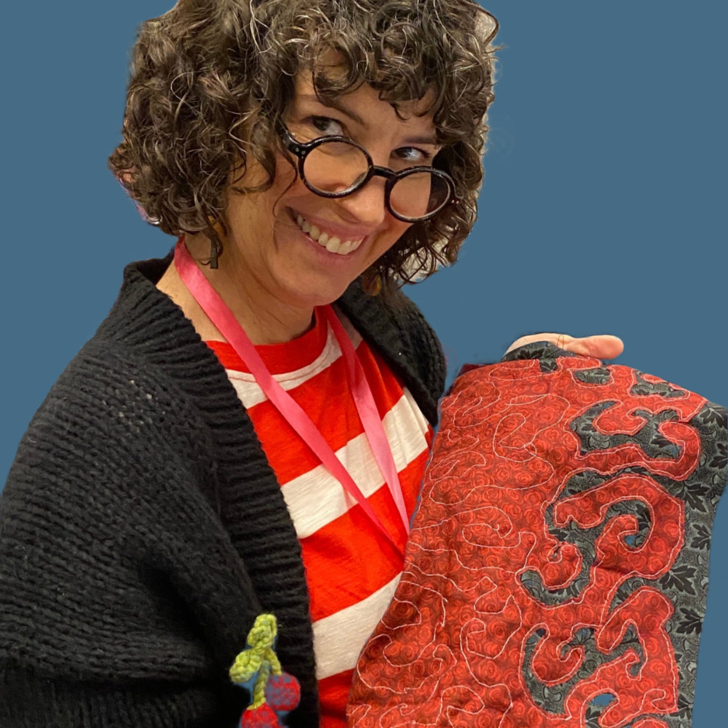 A person wearing a cool sweater wtih cherries crocheted onto it is holding up a fabric cowl they made using reverse applique.