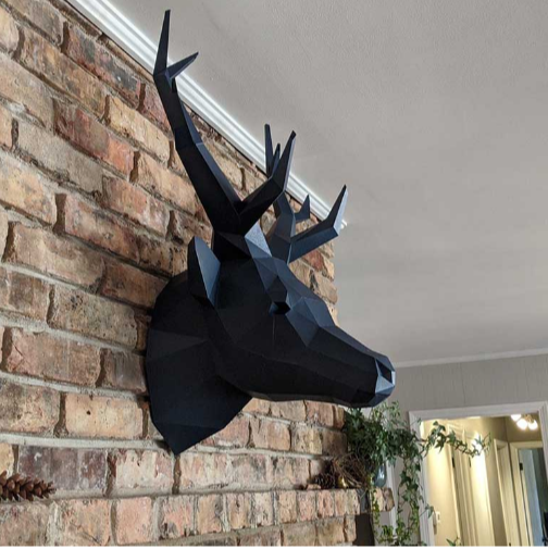An example of a completed deer head paper craft kit. It is hanging on a brick wall.