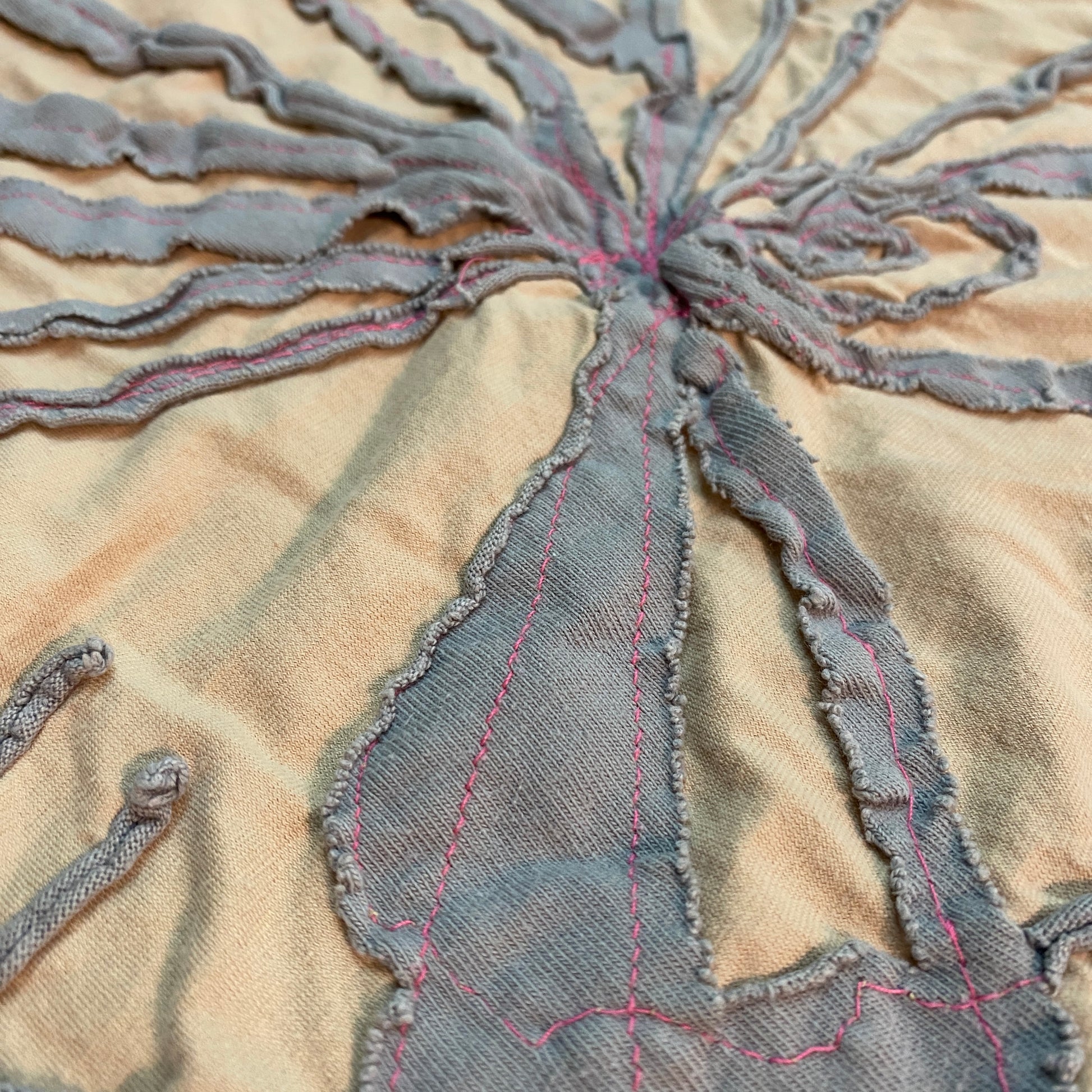 Close up of the peach and grey with hot pink stitching bandana. The edges of the gray fabric curl up because it is a knit fabric. 