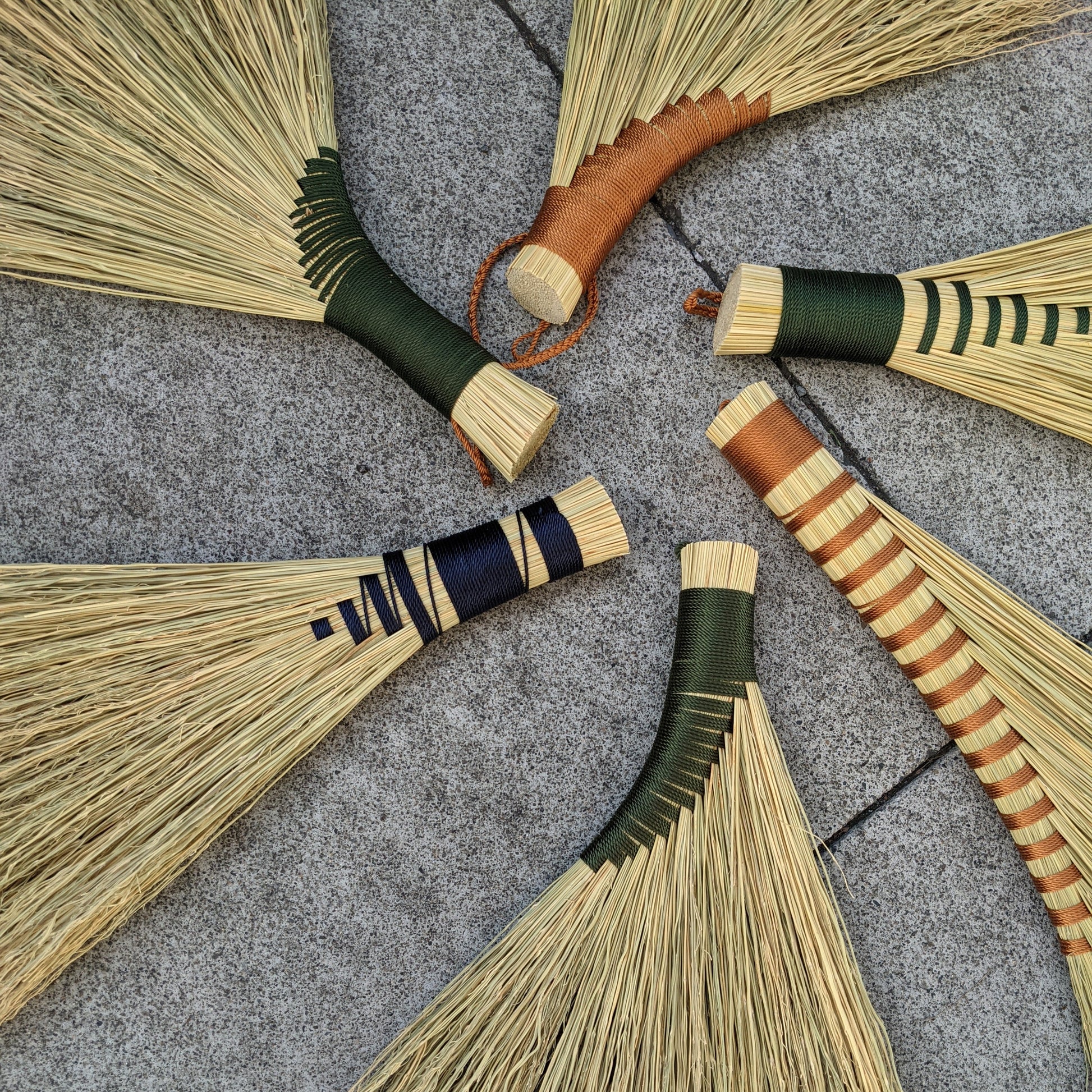 Examples of different types of hand brooms displayed in a circle with their handles pointing inside. There are some with black detail and others with brown detail.