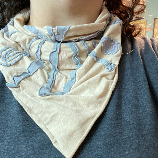 Example of a negative reverse applique bandana worn by a person. The bandana has a peach background with light gray foreground fabric and hot pink stitching. 