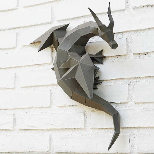An example of a dragon paper craft kit completed and hanging on a white brick wall. 