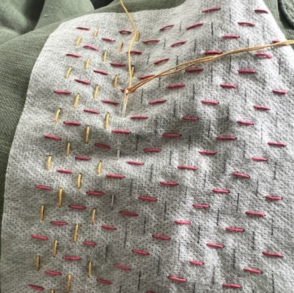 An example of one of the fiber arts sashiko washable mending transfer stitched onto denim with pink and yellow thread. 