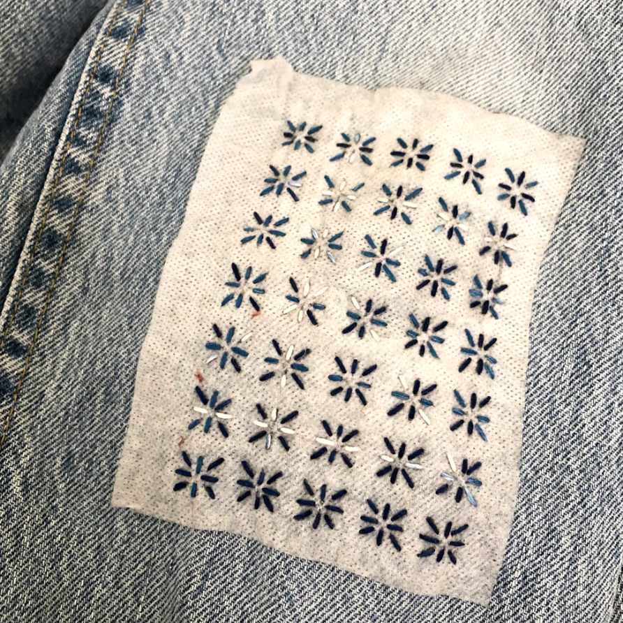 Denim jeans with a visible mend in progress. 