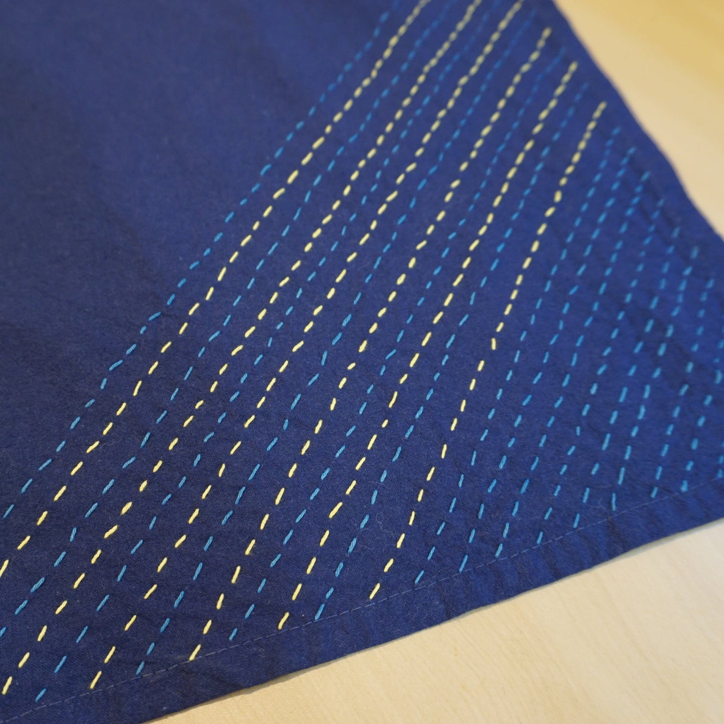 A navy blue tea towel is decorated with lighter blue and yellow stitches.