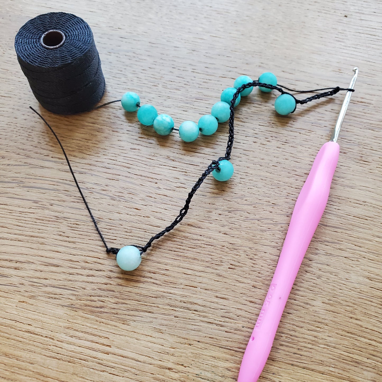 Supplies for the crochet necklace class. String, beads and a crochet hook with a pink handle. 