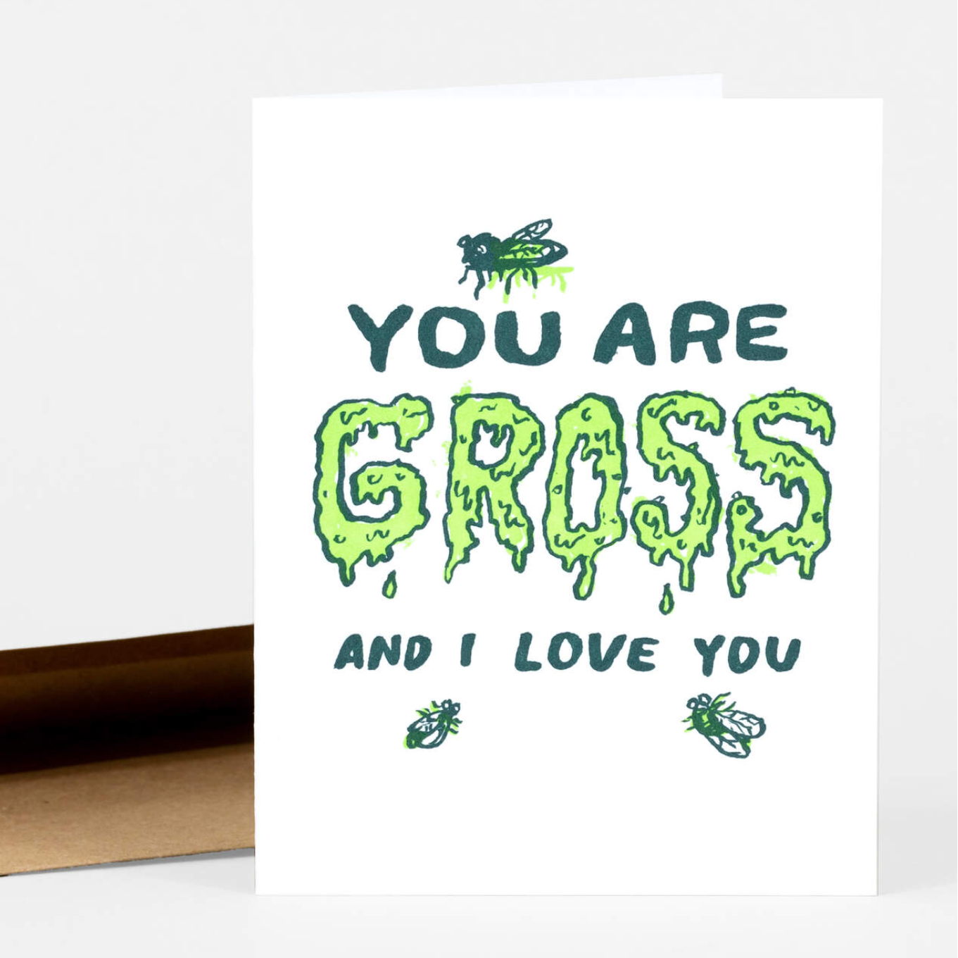 A letterpress greeting card that says "you are gross and I Love you." The word gross is written in dripping neon green letters. There are three flies gathering on it. 