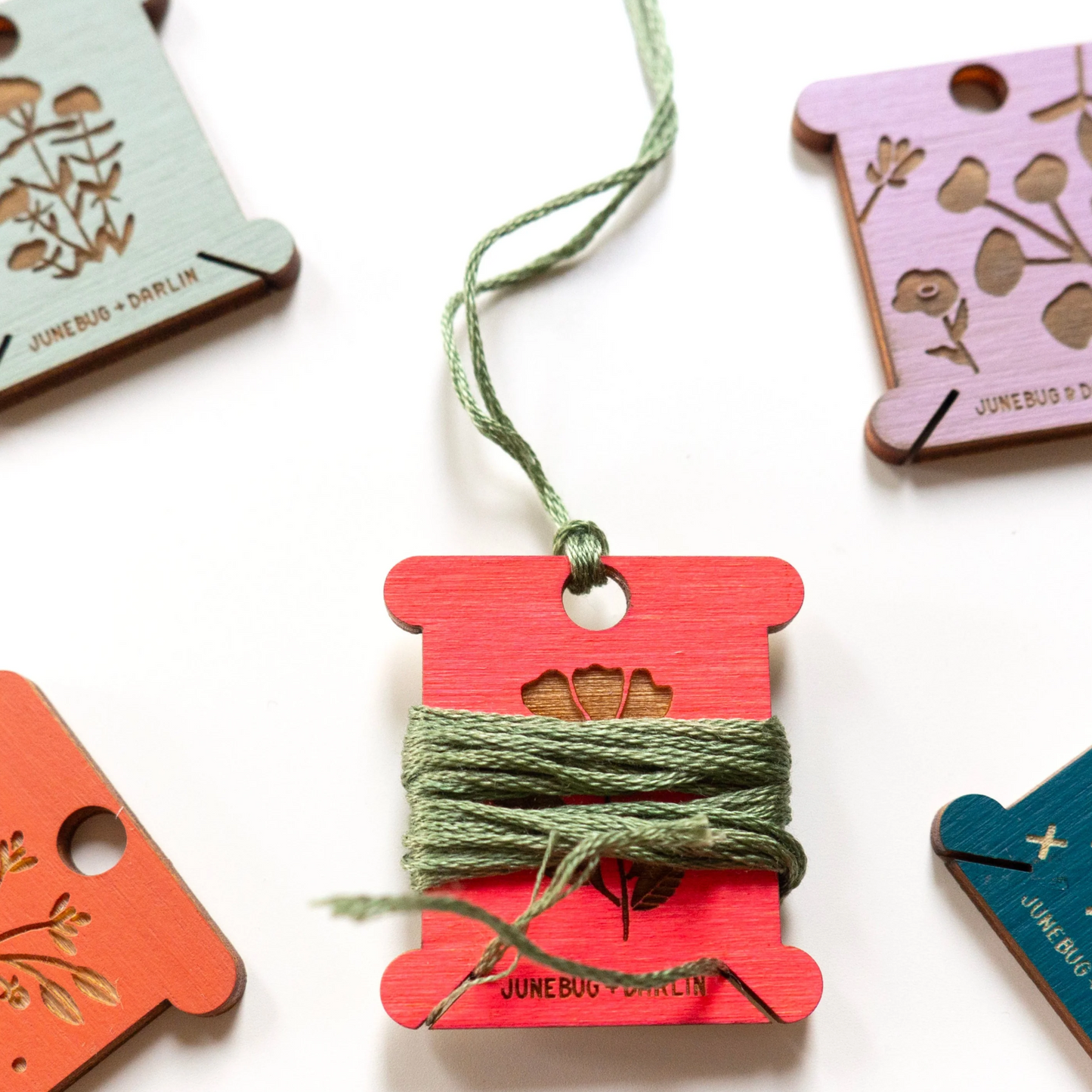 A photo of five different floss holders by junebug and Darlin. One in the middle has floss wrapped around it and one also tied through the hole at the top. 