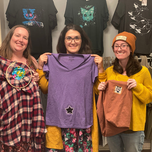 Three people holding up their reverse applique hand sewing projects that they made in class at Monster.