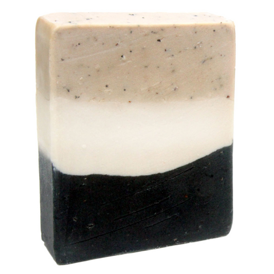 A bar of handmade vanilla chai scented soap with a layer of black color at the bottom, a layer of beige with speckles at the top and the center a solid off-white color. 
